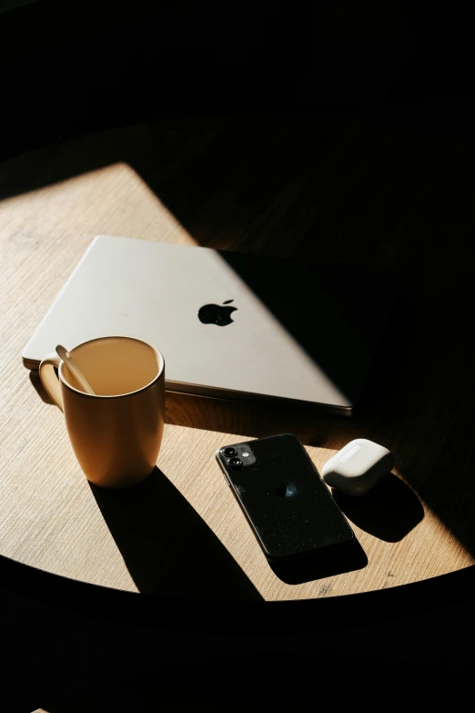 a laptop and cell phone are on the table next to a cup