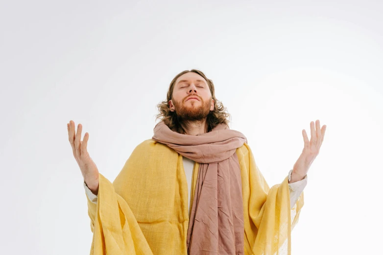 a man in yellow robe and brown scarf standing with his hands outstretched