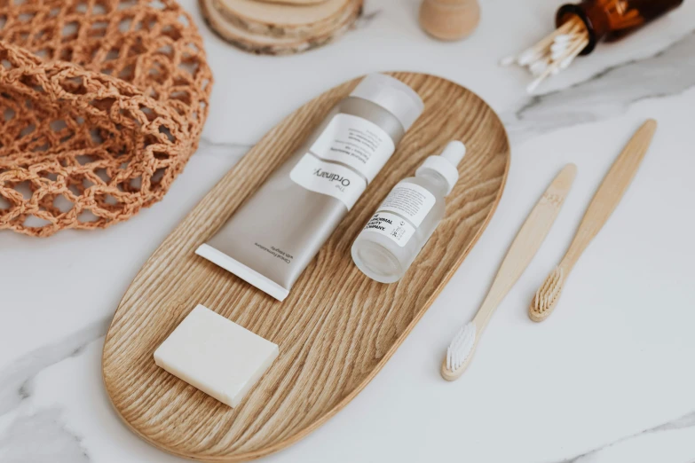 a wooden tray containing some toothbrushes, a bottle of liquid and some white containers