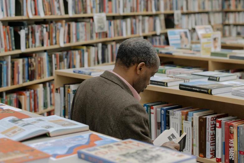 a man reading a book while standing in front of a long liry shelf