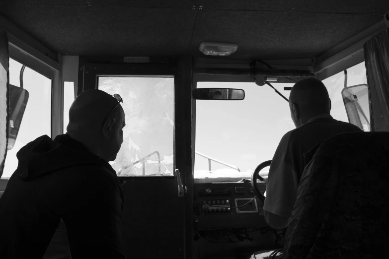 two men sit at the wheel of a bus looking out the window