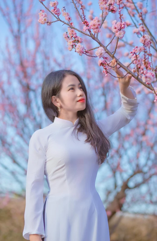 young woman in white dress looking up at a flower filled tree