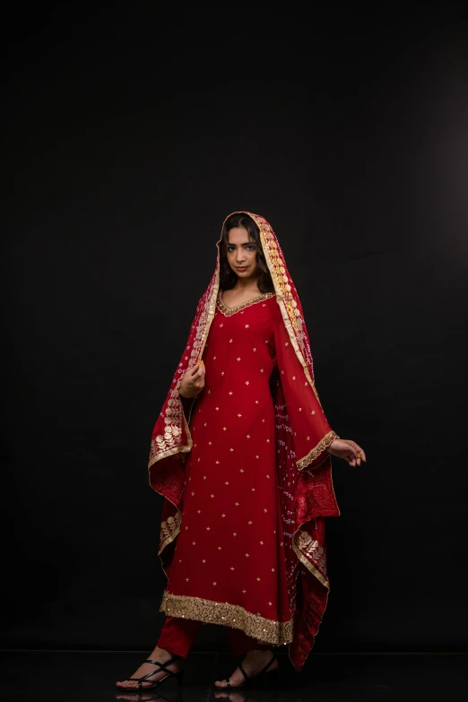 the woman wearing a red dress and cape stands in front of a dark backdrop