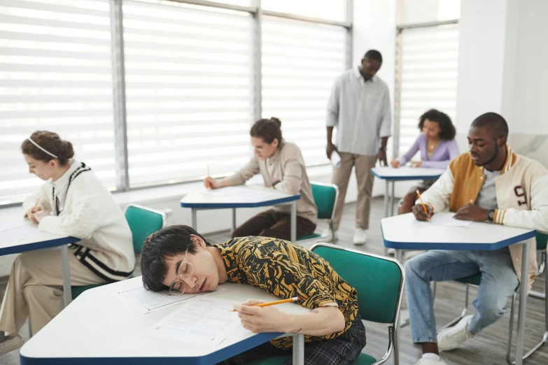 a boy sleeps on his desk while students draw on paper