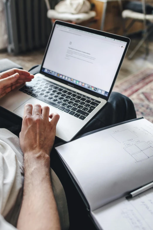 person sitting with laptop on lap top and book open