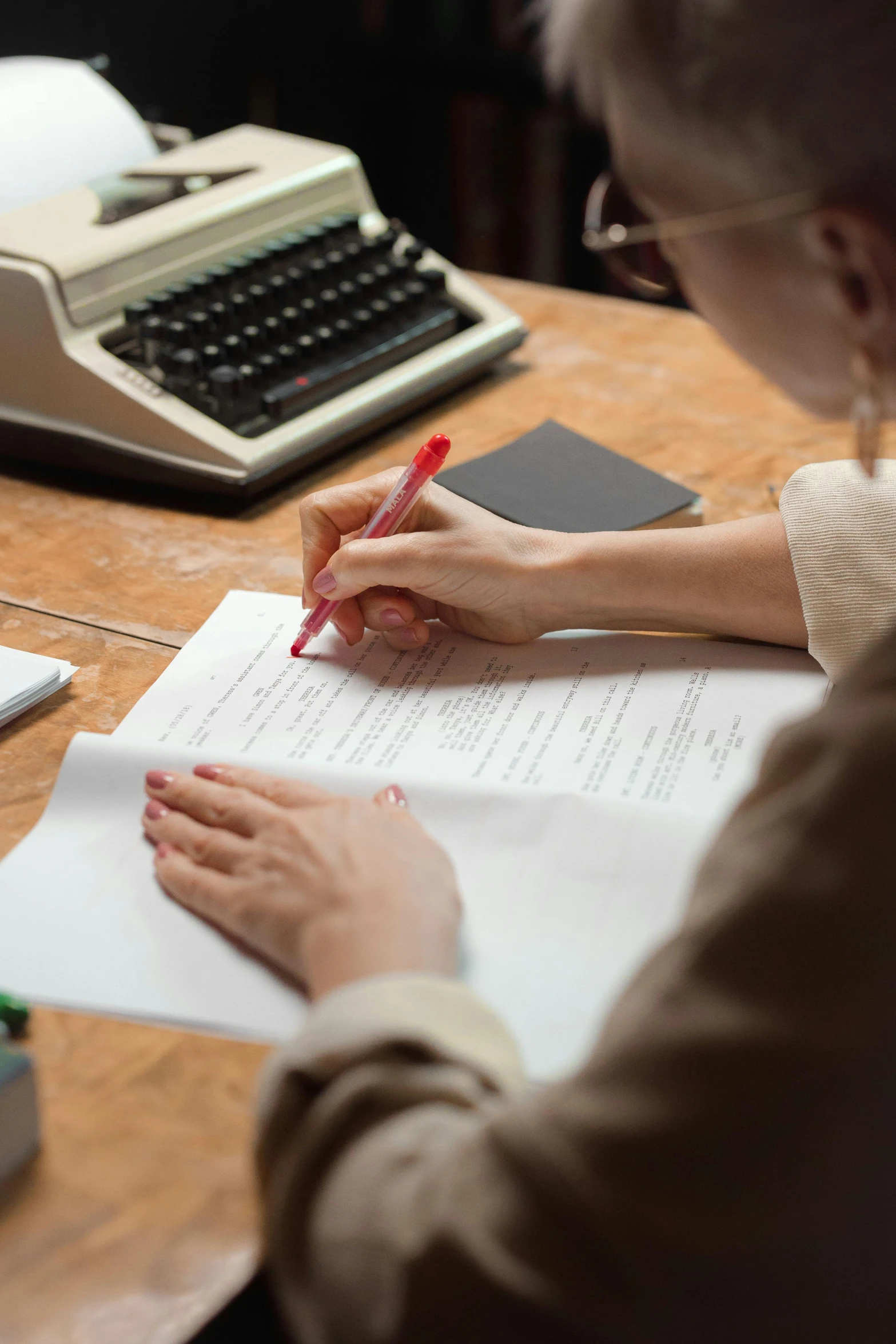 an older woman writes in her book while using a typewriter