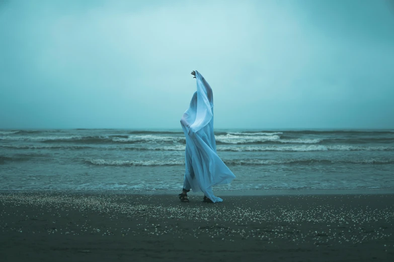 a woman is standing on the beach looking out to sea