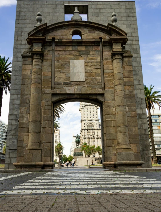 large stone archway with palm trees and buildings behind