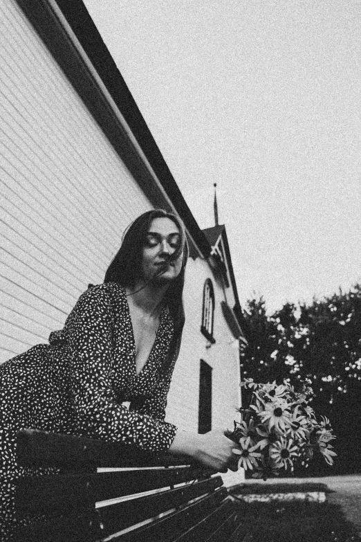 black and white image of a woman leaning against the outside of a house