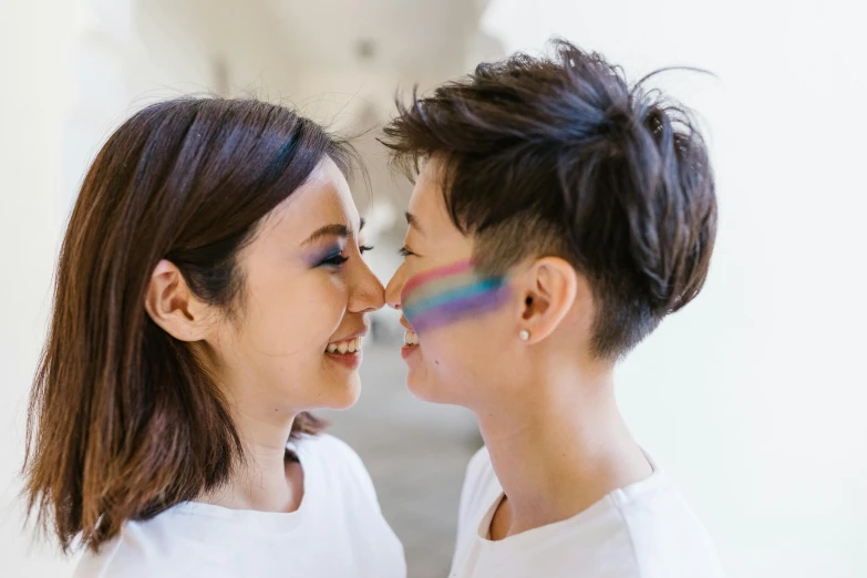 two young women in white shirts, each with their face painted with rainbows