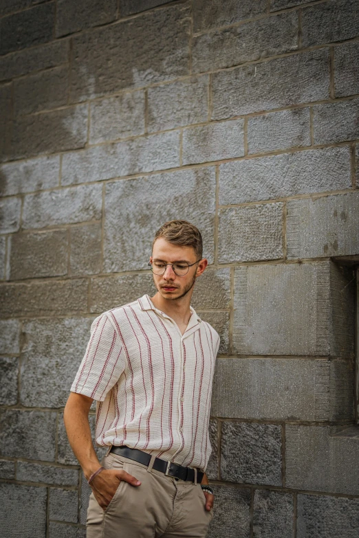 a guy standing by a brick wall looking into the camera