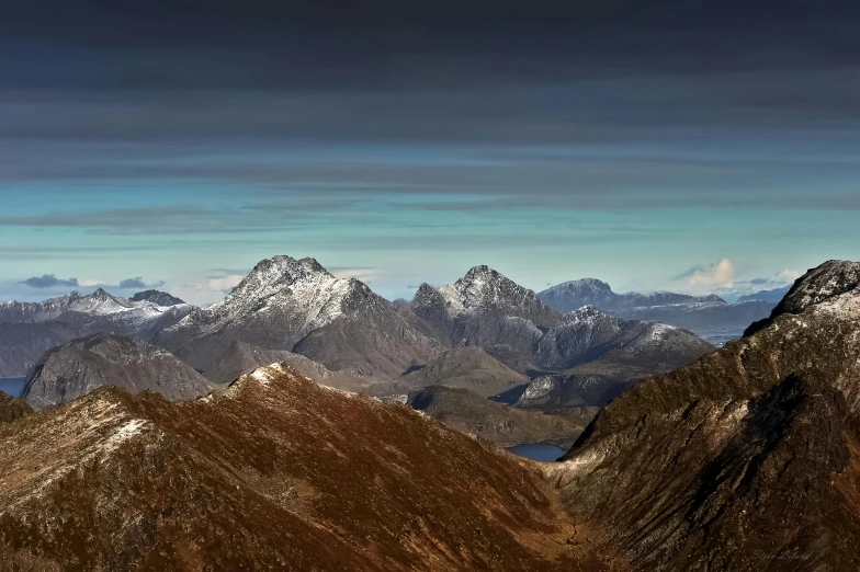 several snow capped mountains sit under a cloudy sky