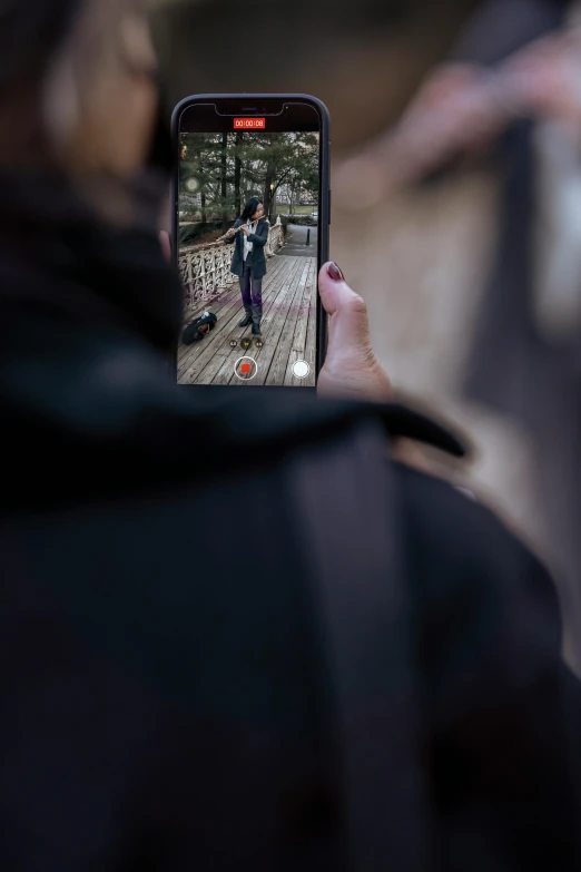 person taking a picture of a person standing on the ground on a dock with their cell phone