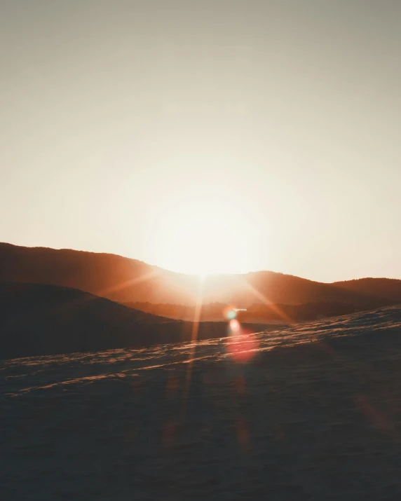 the sun shining through some hills with two snowboards