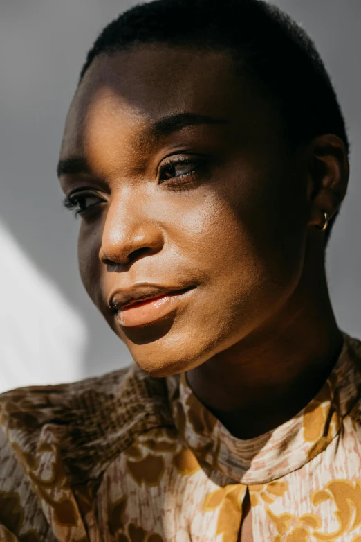 an african woman with one eye shut and dark skin wearing a yellow patterned shirt