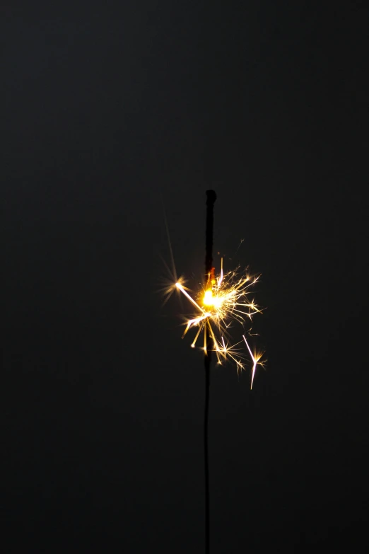 a sparkler is glowing yellow while it appears to be in the dark