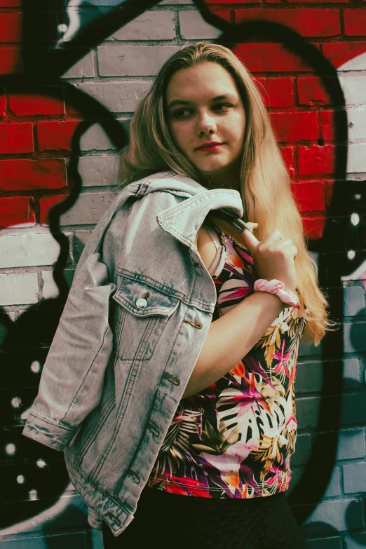 a woman standing in front of a brick wall with a jean jacket