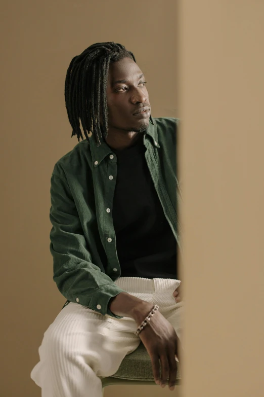 a man in a green jacket and white pants sitting on a chair