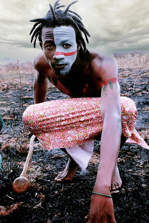 a man with a painted face sitting in the middle of a dirt field
