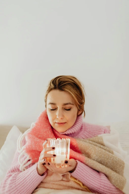 a girl sitting on top of a bed while holding a candle