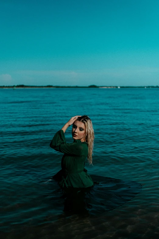 a woman in a green dress stands in the ocean