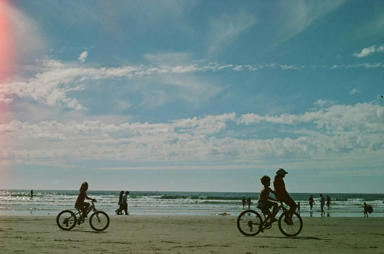 a couple of people ride bicycles on a beach