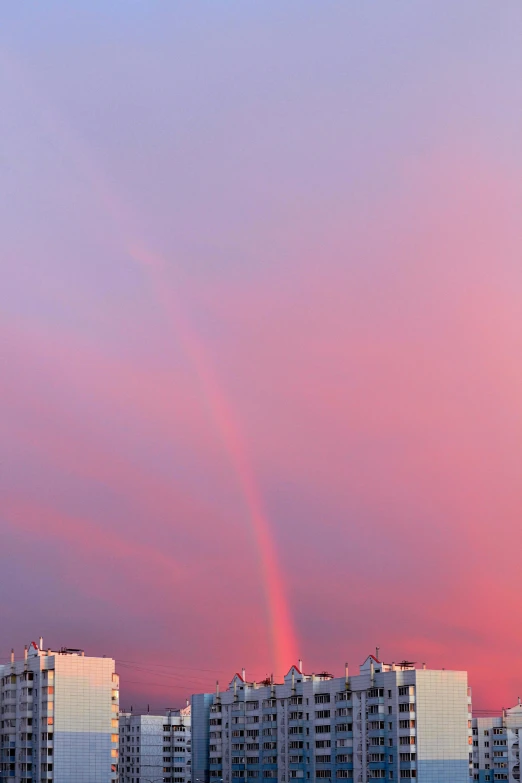 an upward view of city buildings and a rainbow in the sky