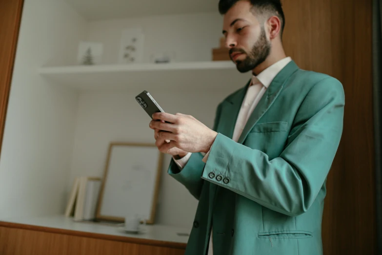 a bearded man in a teal green suit and tie checking his cellphone