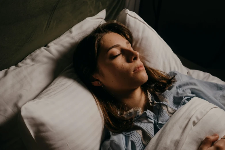 a young woman lies in bed, snuggling with a blanket