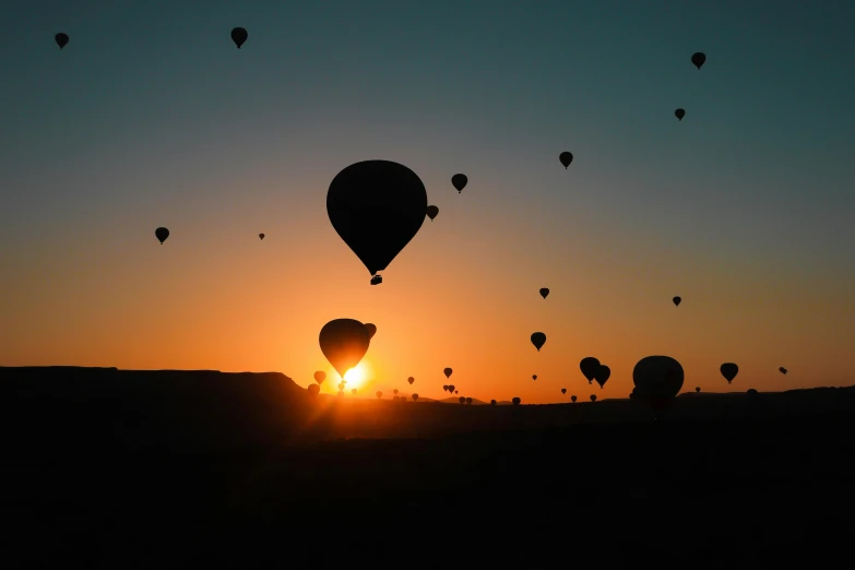 many balloons being released into the sky over a field at sunset