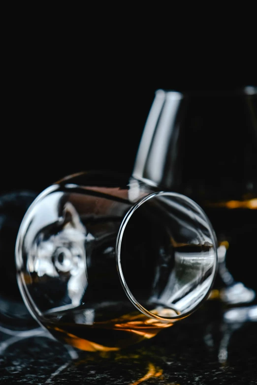 two glasses of whiskey sit on a dark surface