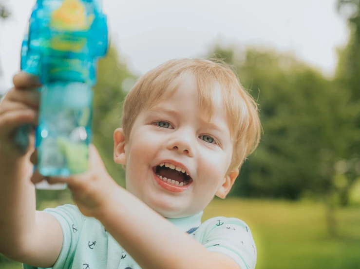 a boy with red hair holding up a plastic bottle