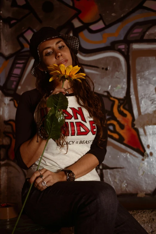 woman holding yellow flower in front of graffiti covered wall