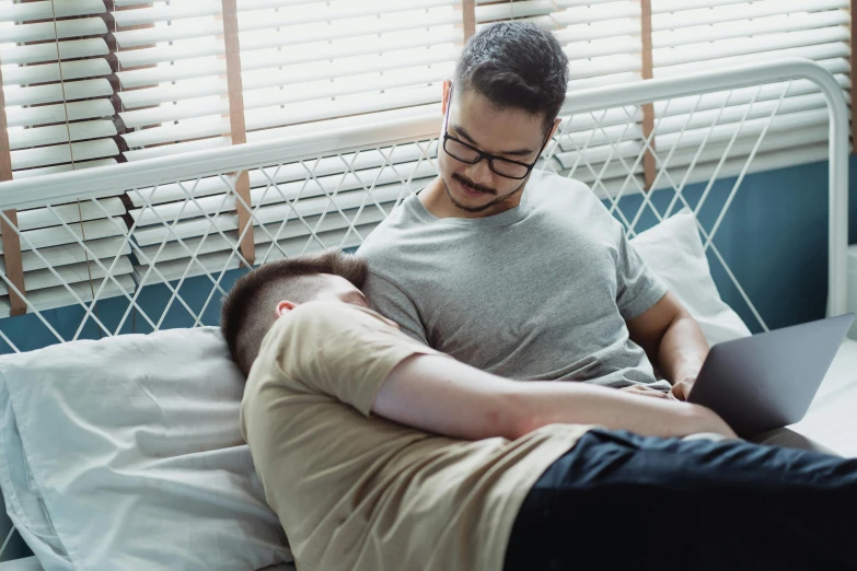 man sitting on bed next to another man using laptop