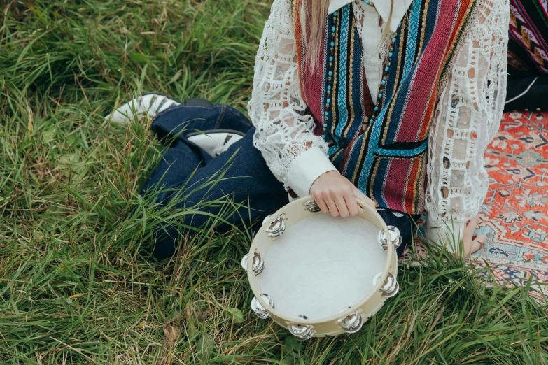 a woman is sitting in the grass and holding a tamboure