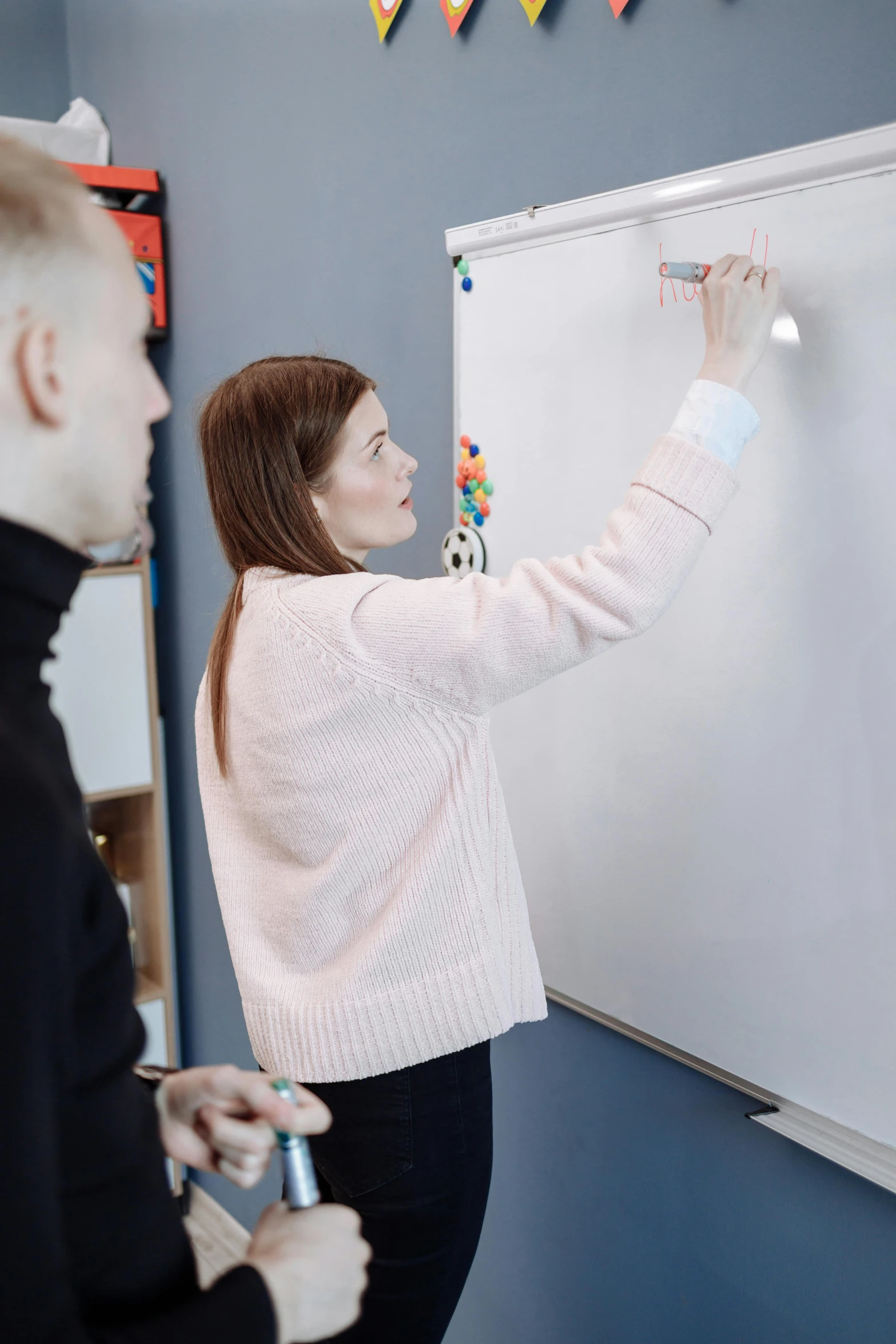 two people writing on a white board in the room