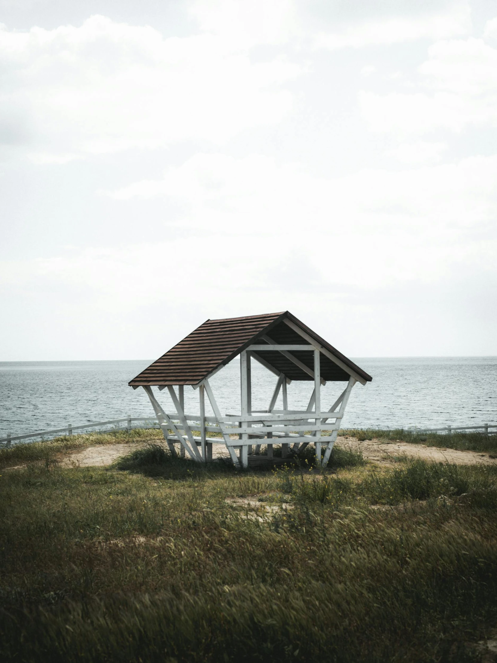 a shelter with a striped roof sitting in the grass on the shore