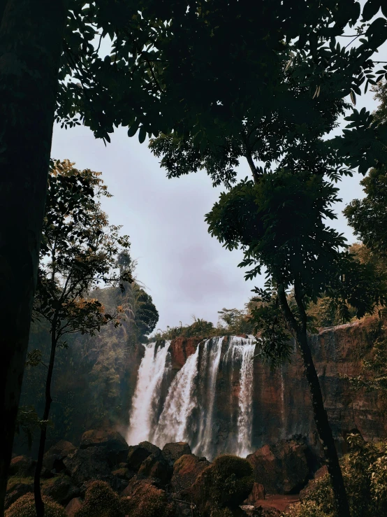 two people in the distance, standing by trees near a waterfall