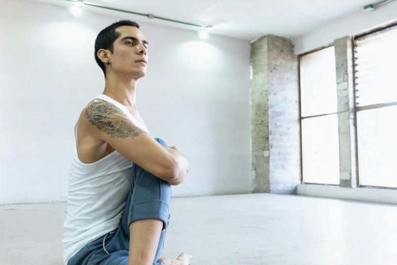 a male in jeans and a tank top is sitting on a white floor