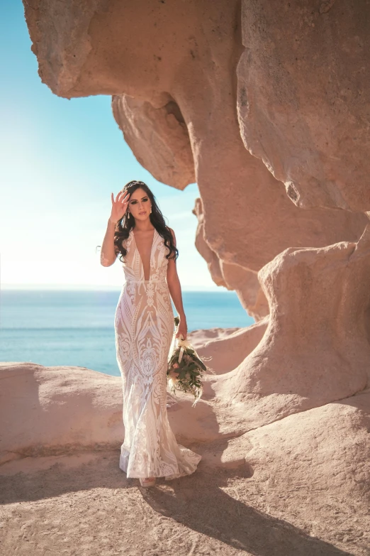 a woman wearing a wedding dress in front of rocks