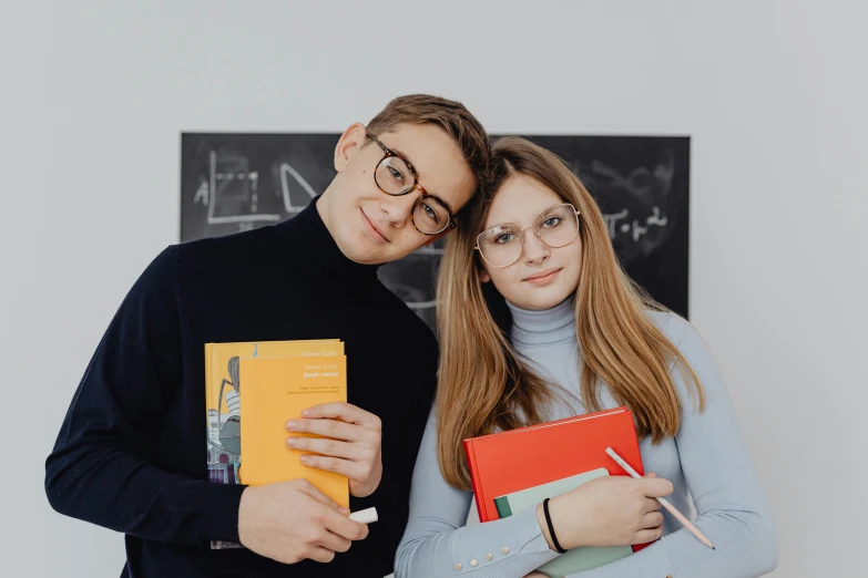 man and woman posing in front of chalkboard holding books