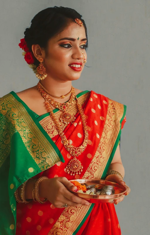 a woman in a traditional red and green indian dress holds a plate with food