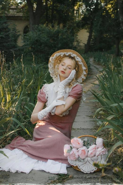 a young lady in a dress and bonnet sits next to a basket of flowers