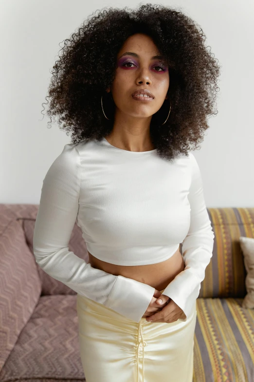 an afro woman in white top poses in front of a couch