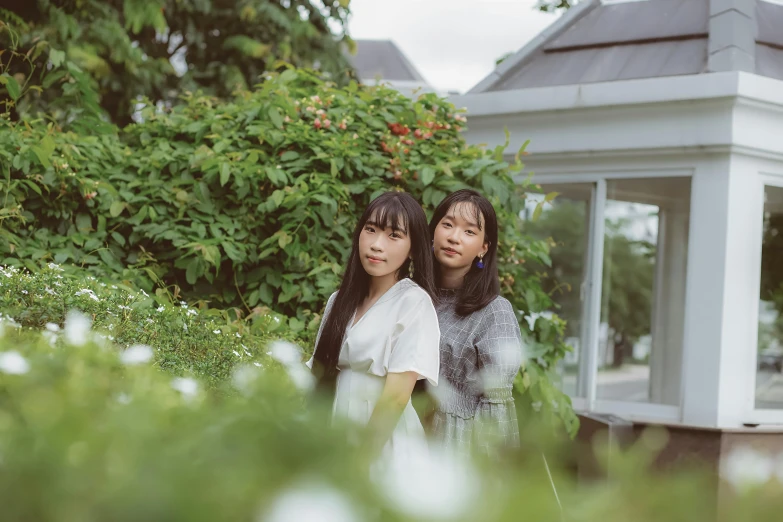 two asian women standing near each other in front of a gazebo