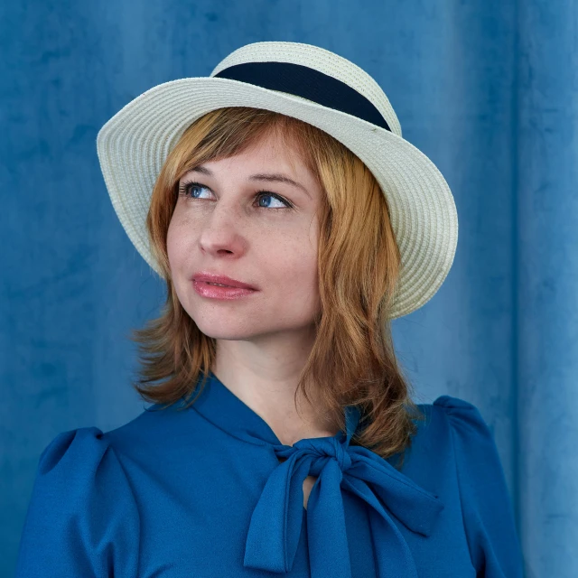 a woman wearing a white hat in front of a blue curtain