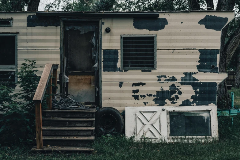 an old run down mobile home next to a grassy field