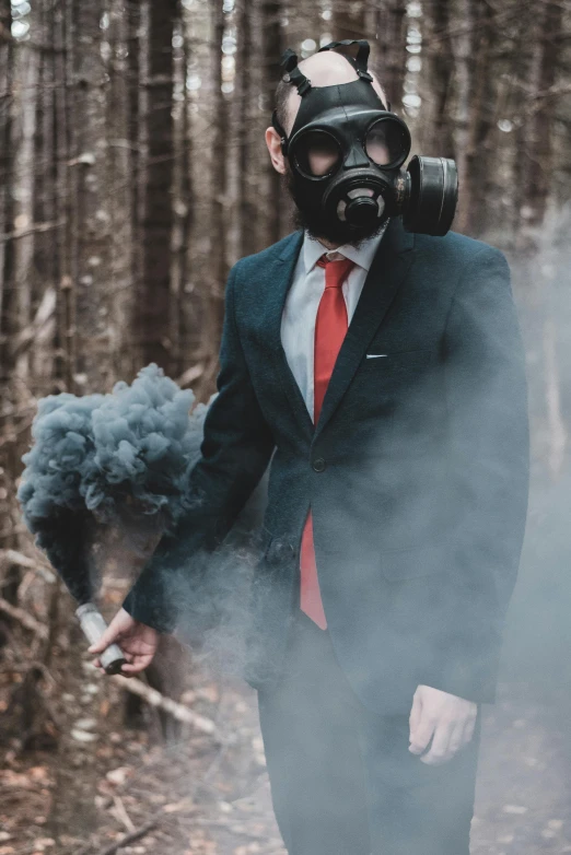 a man wearing a gas mask smokes his cigarette while standing in the woods