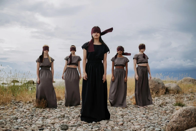 five women wearing long black and brown dresses standing on rocks