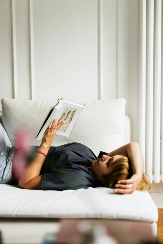 a woman lying on a couch reading a book